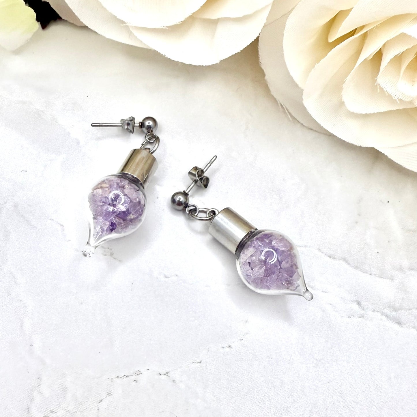 Pair of stud earrings with glass vials filled with shards of amethyst showing detail of ball stud and butterfly closure