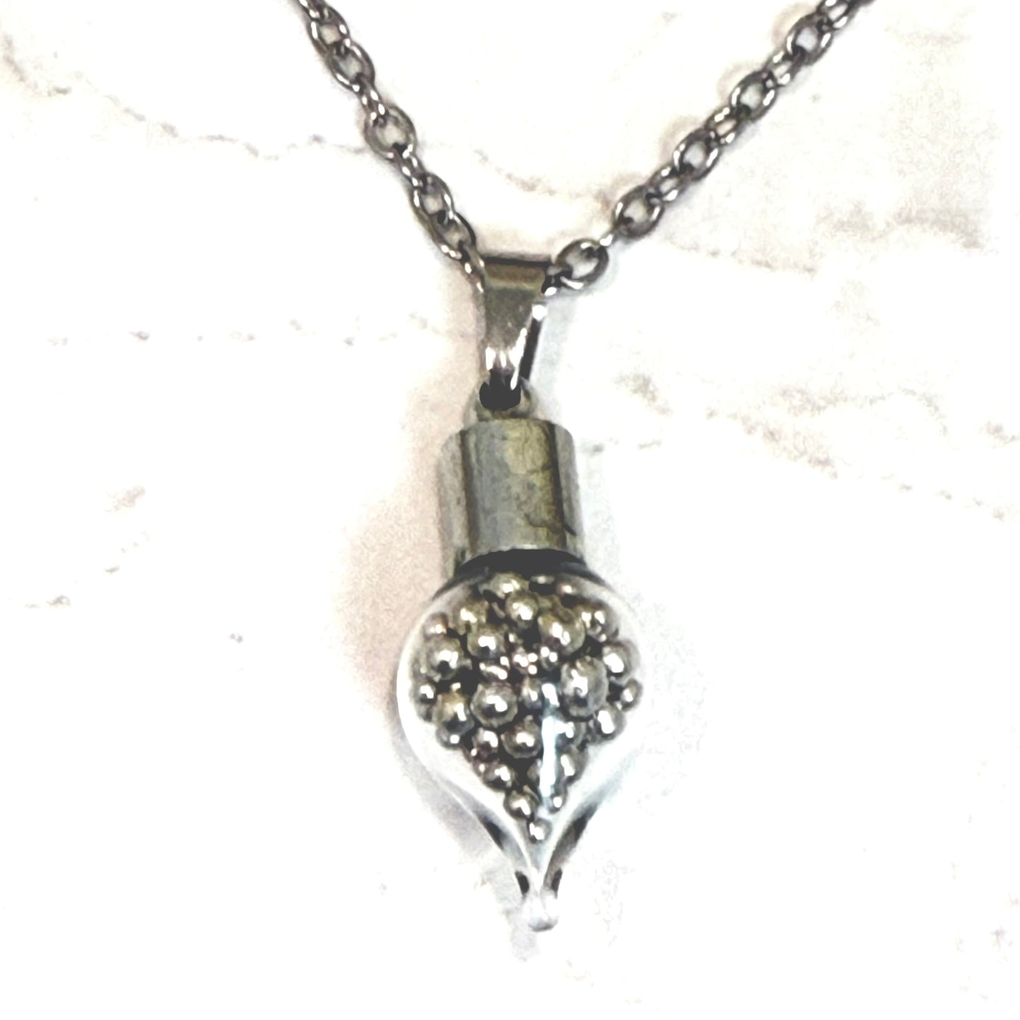 detail of glass teardrop pendant filled with pure tine balls on chain
