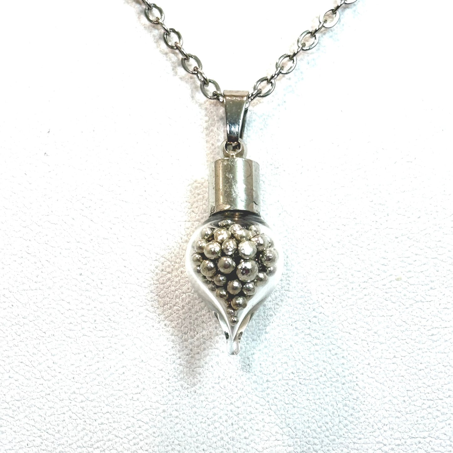 front view of glass pendant filled with balls of pure tin