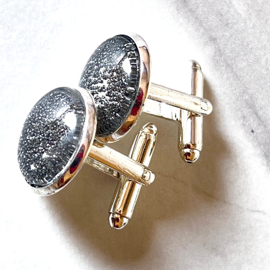 close up silver iron anniversary cufflinks showing iron filings behind glass cabochon